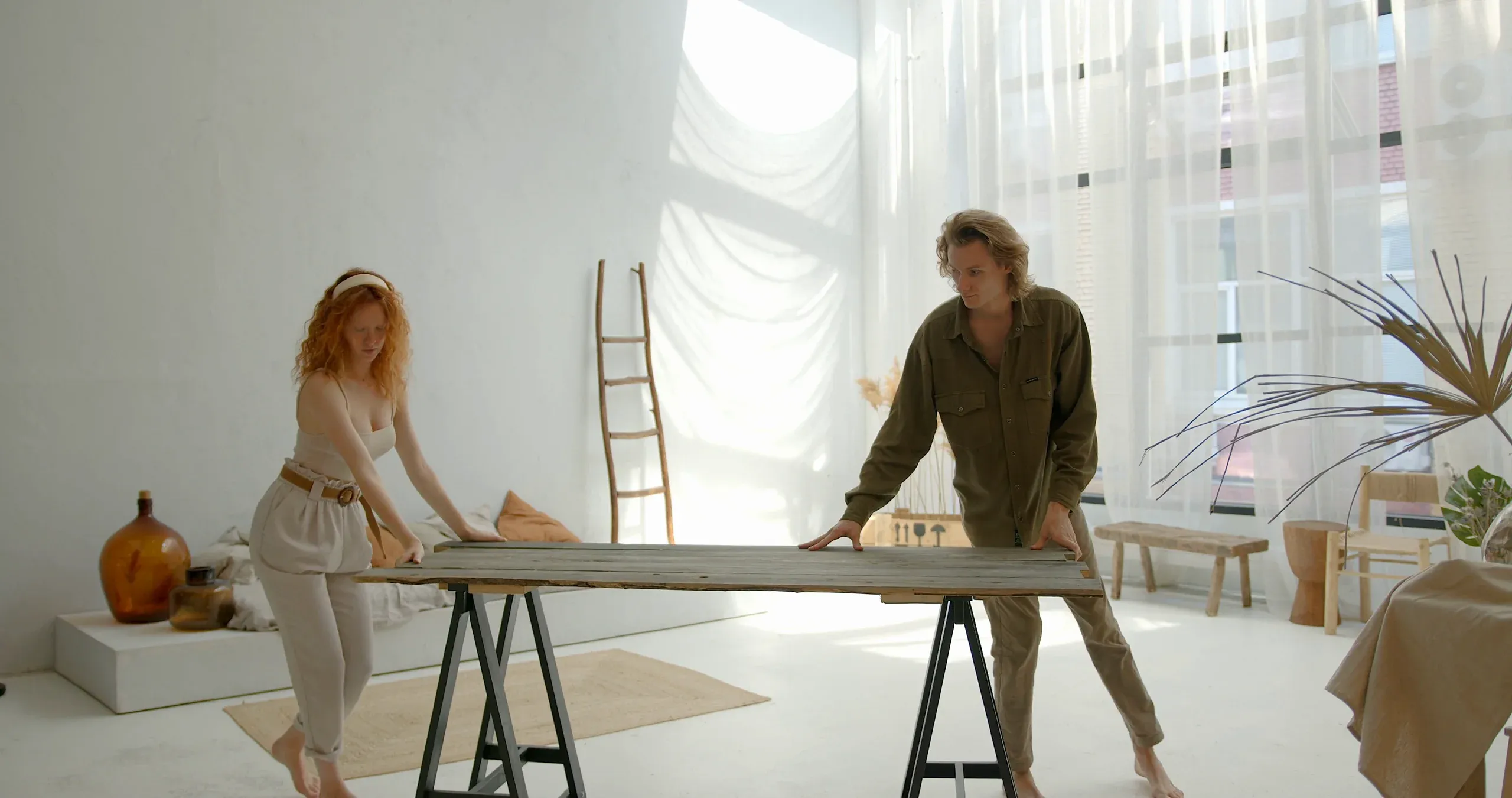 Two people setting a wooden table on trestles in a bright white studio
